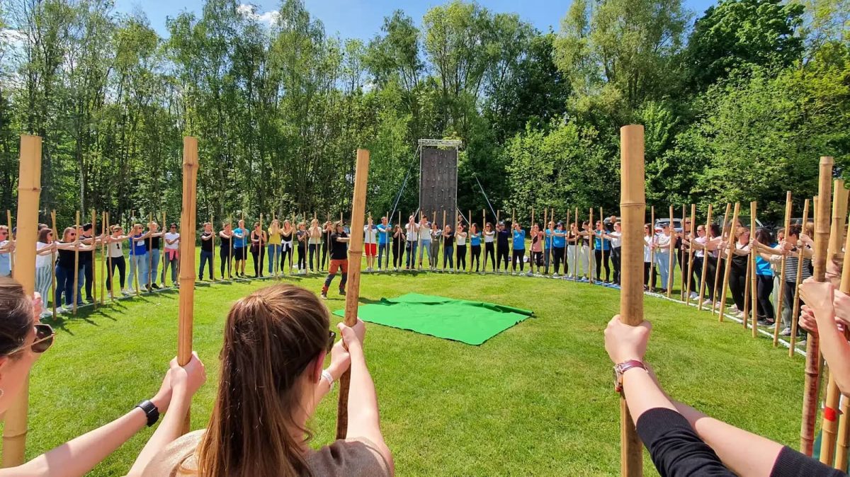 Grand cercle de participants tenant des bâtons de bambou lors d'un teambuilding Xtreme Events