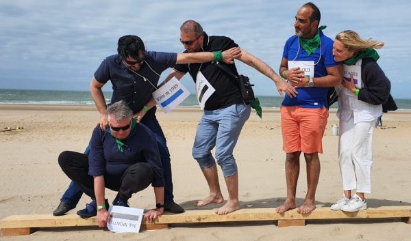 Groupe en équilibre sur une planche lors d'un défi de cohésion sur la plage