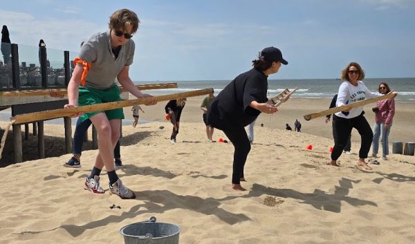 Participants portant de longues perches en équilibre lors d'un relais sur la plage