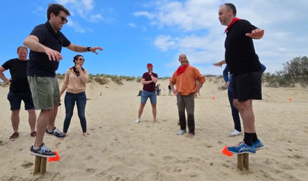 Participants en équilibre sur des plots en bois lors d'un défi sur la plage