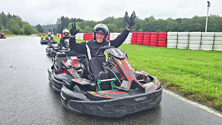 Pilote levant les bras dans son kart n° 11 sur la piste mouillée