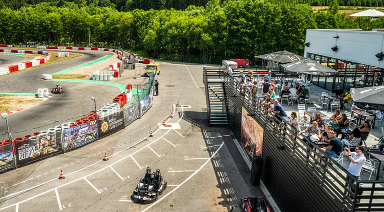 Terrasse en hauteur du karting avec tables et parasols, au-dessus de la piste