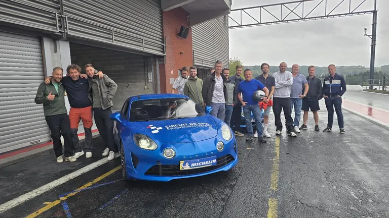 Alpine A110 bleue des baptêmes de piste Xtreme Events dans la pitlane du Circuit de Spa-Francorchamps, entourée d’un groupe d’entreprise