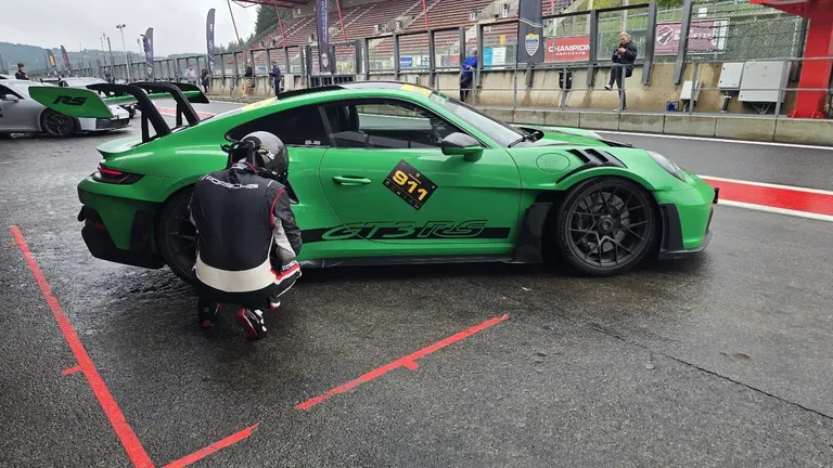 Pilote en combinaison auprès d’une Porsche 911 GT3 RS verte dans la pitlane du Circuit de Spa-Francorchamps, avant un stage de pilotage