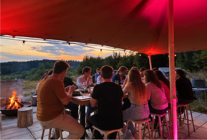 Dîner convivial sous l’abri éclairé du Woodcamp, avec feu de camp et vue sur les collines